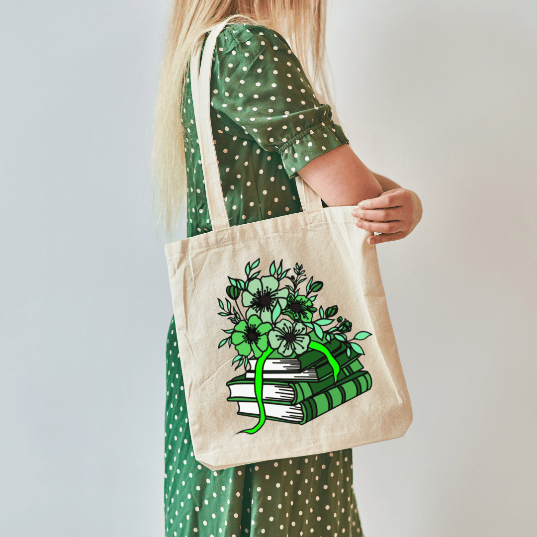 Person holding a tote bag with a green floral and book design on a plain background