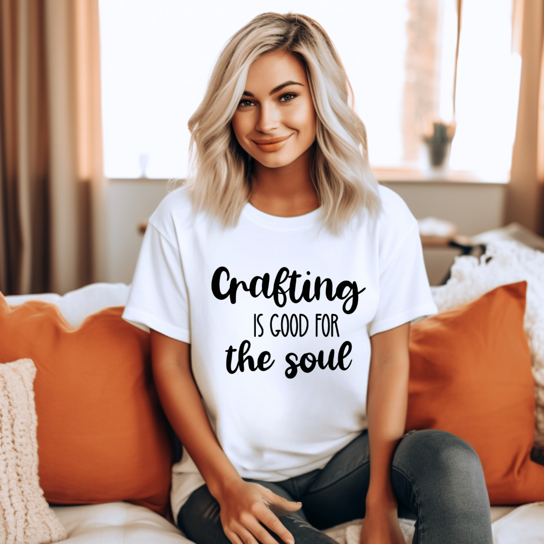 Woman wearing a white t-shirt with 'Crafting is good for the soul' text in a cozy living room.
