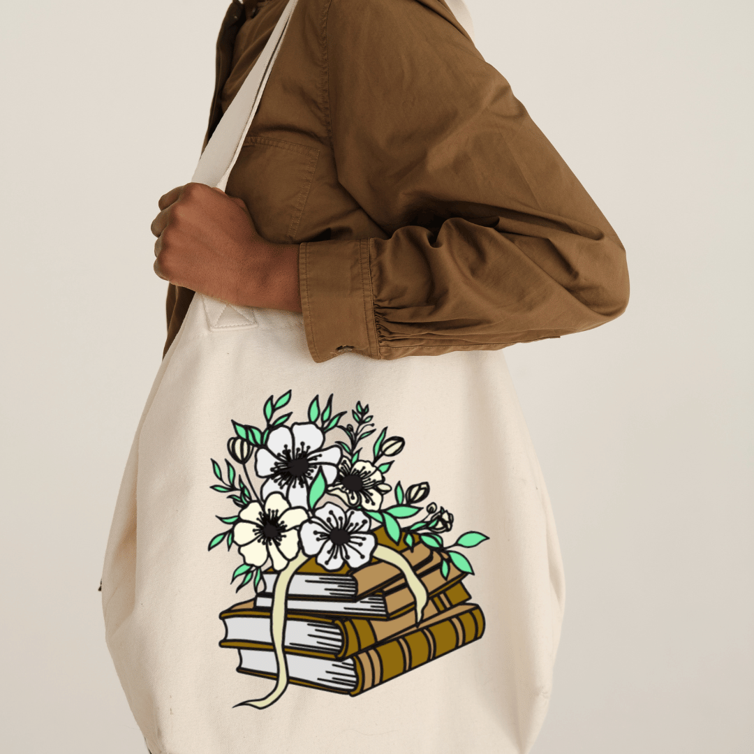 Tote bag with floral and book design held by a person wearing a brown jacket.