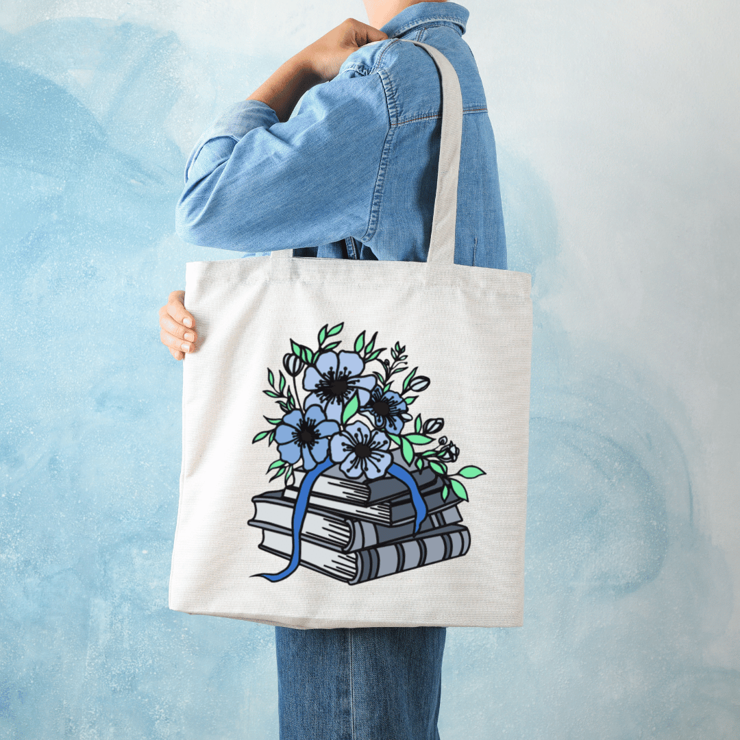 Tote bag with floral and book design held by a person against a light blue background