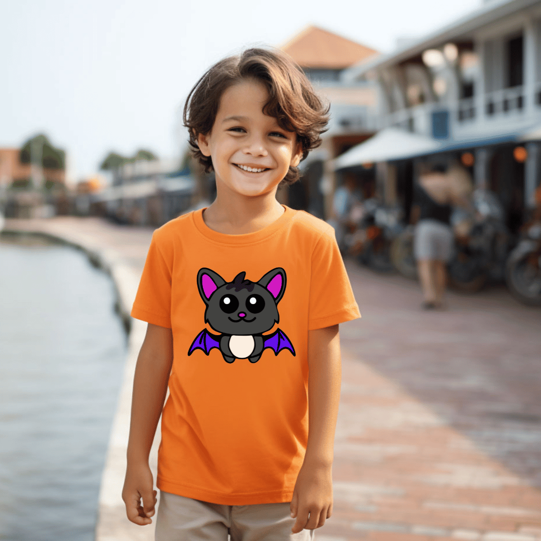 Child wearing an orange t-shirt with a cartoon bat design, standing on a waterfront promenade.