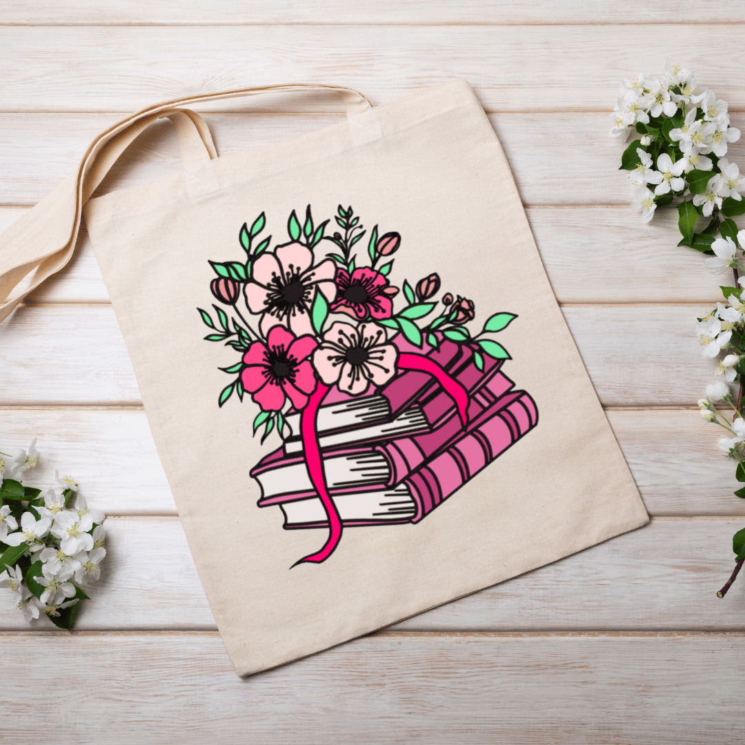Beige tote bag with a pink floral and book design on a wooden surface