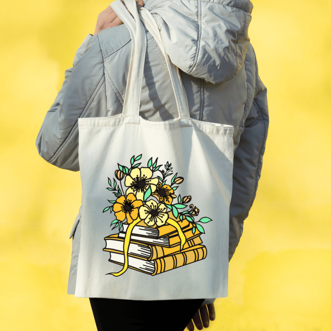 Person holding a tote bag with floral and book design against a yellow background