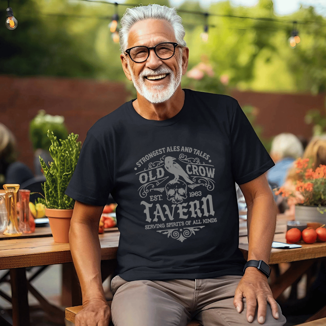 Man wearing a black t-shirt with 'Old Crow Tavern' design, sitting outdoors.