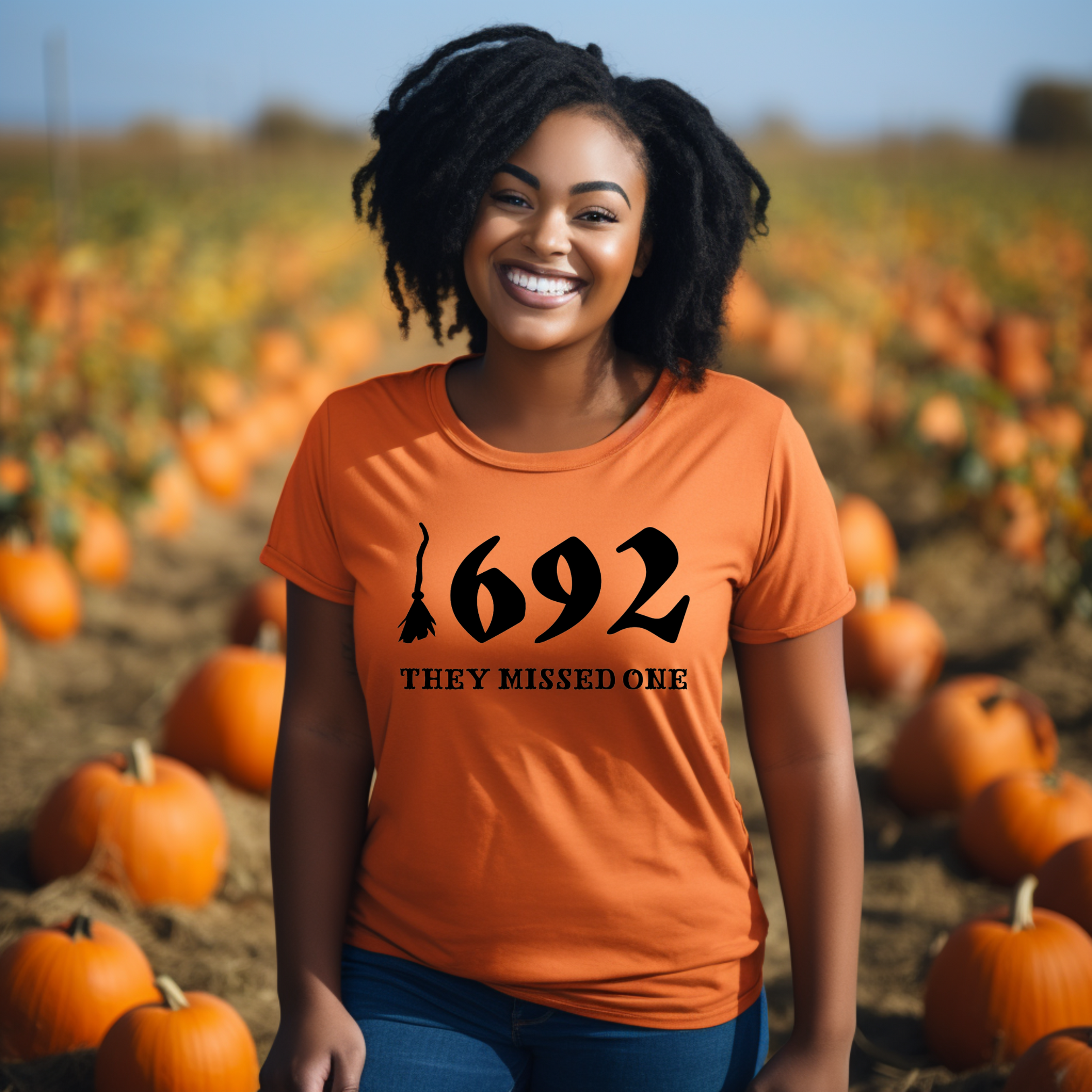 A person in a pumpkin patch wearing an orange t-shirt with the text '1692 THEY MISSED ONE' on it.