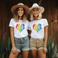 Two women wearing 'PRIDE' t-shirts with rainbow hearts outdoors.