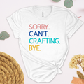 A white t-shirt with the text 'Sorry. Can't. Crafting. Bye.', each line with a different color text.