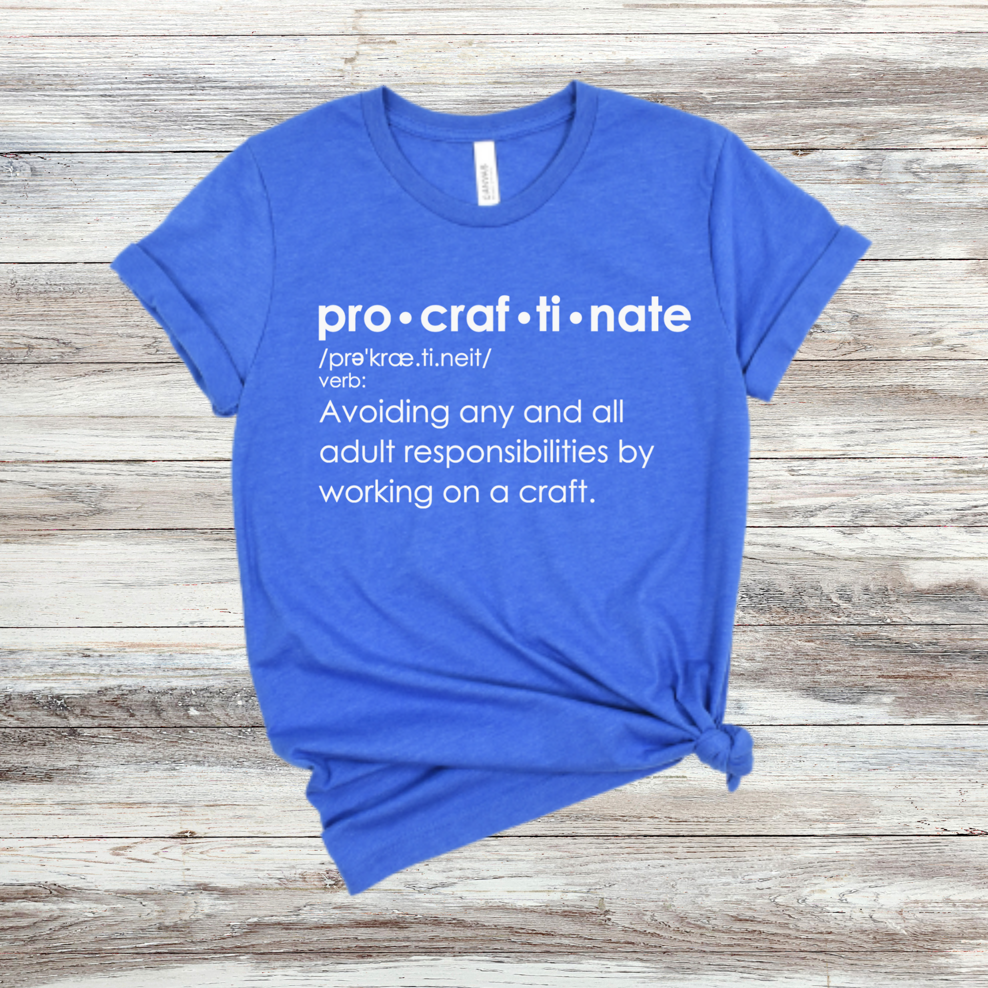 A blue t-shirt with the text 'pro-craft-i-nate' printed in white, defineing the word as 'Avoiding any and all adult responsibilities by working on a craft.'.