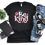 Black t-shirt with 'Always Be Kind' text, jeans, sneakers, and a notebook on a white surface.