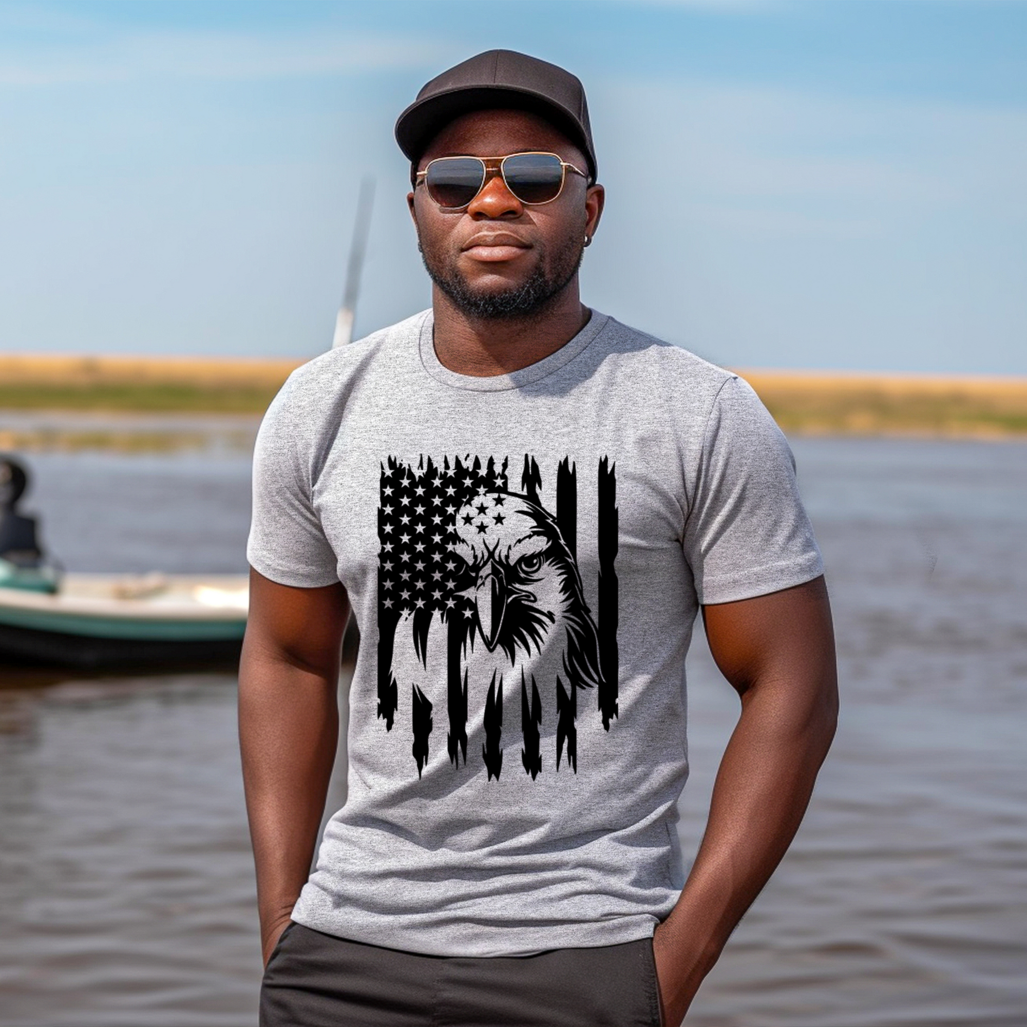 Man wearing a gray t-shirt with an eagle and American flag design, standing by a body of water.