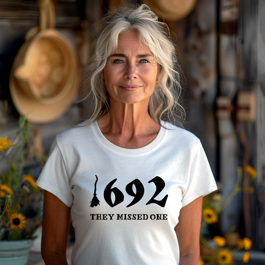 A person with white-blonde hair wearing a white t-shirt with the text '1692 THEY MISSED ONE' on it.