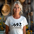A person with white-blonde hair wearing a white t-shirt with the text '1692 THEY MISSED ONE' on it.