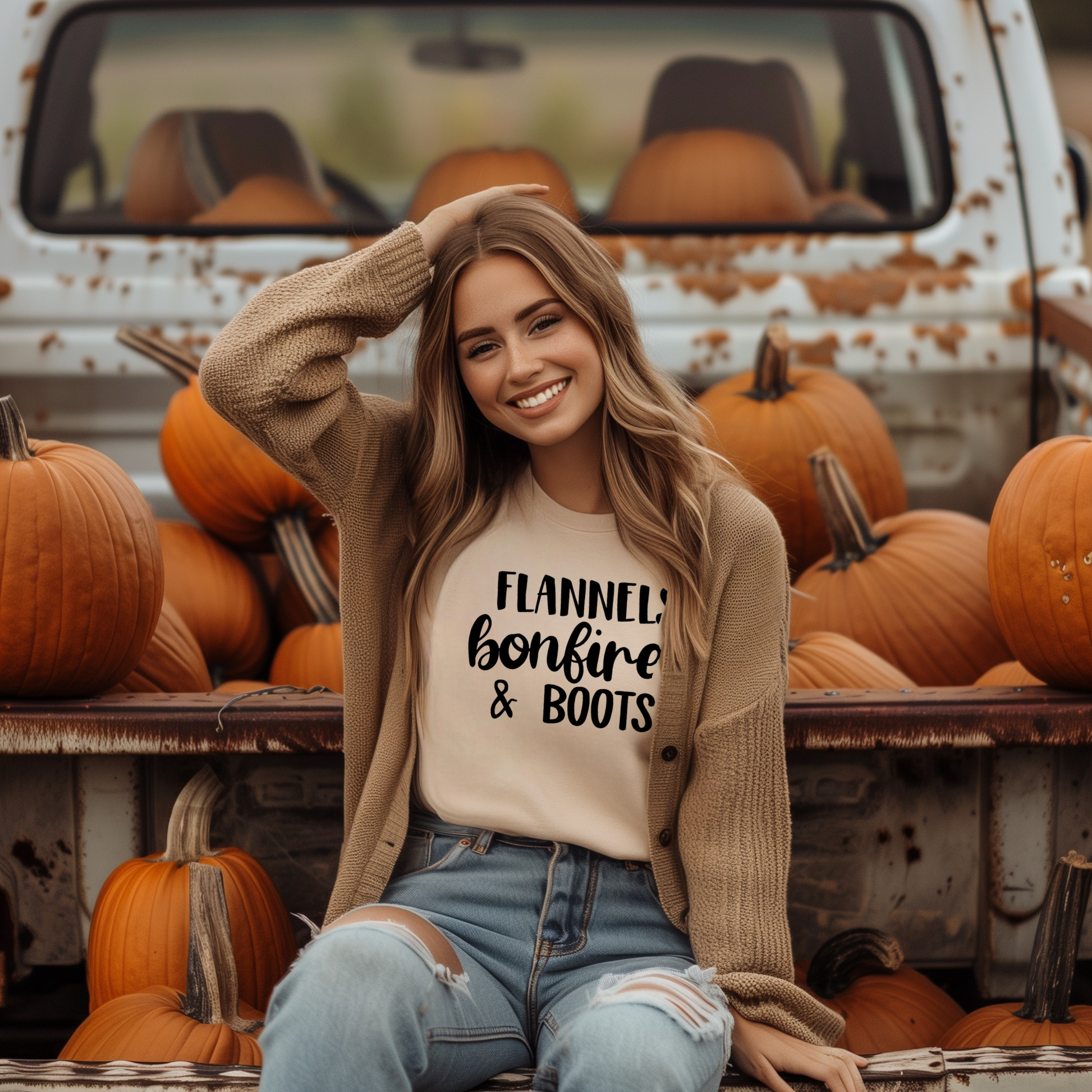 A woman smiling and sitting in a truck, wearing a green t-shirt with the text 'FLANNELS BONFIRES & BOOTS' printed on it, surrounded by pumpkins.