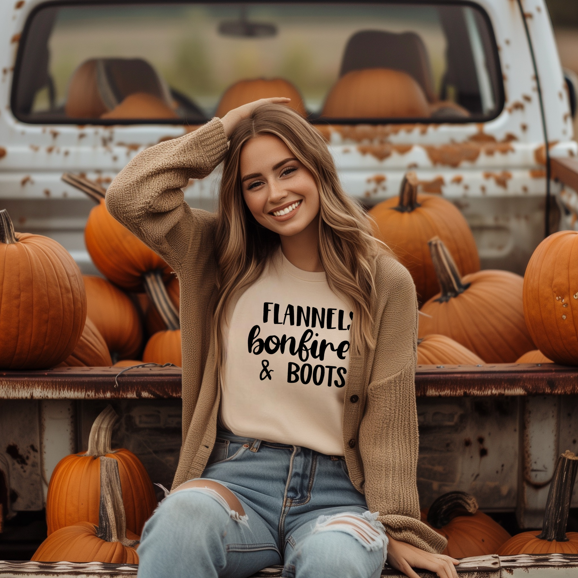 A woman smiling and sitting in a truck, wearing a green t-shirt with the text 'FLANNELS BONFIRES & BOOTS' printed on it, surrounded by pumpkins.