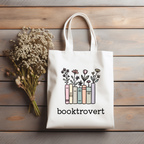 Tote bag with 'booktrovert' design on a wooden surface with flowers.