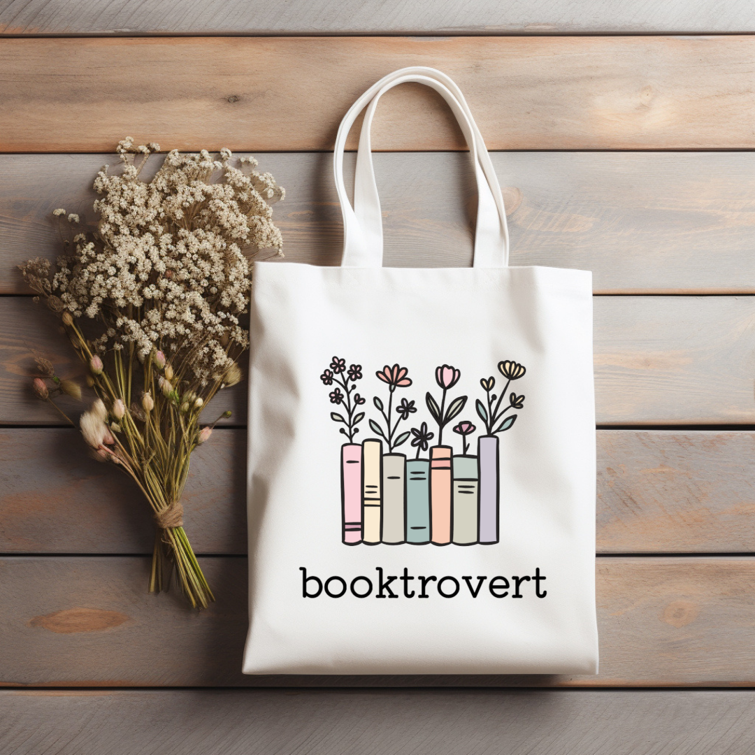 Tote bag with 'booktrovert' design on a wooden surface with flowers.