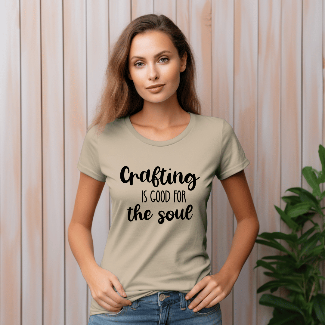 Woman wearing a beige t-shirt with 'Crafting is good for the soul' text against a wooden panel background.