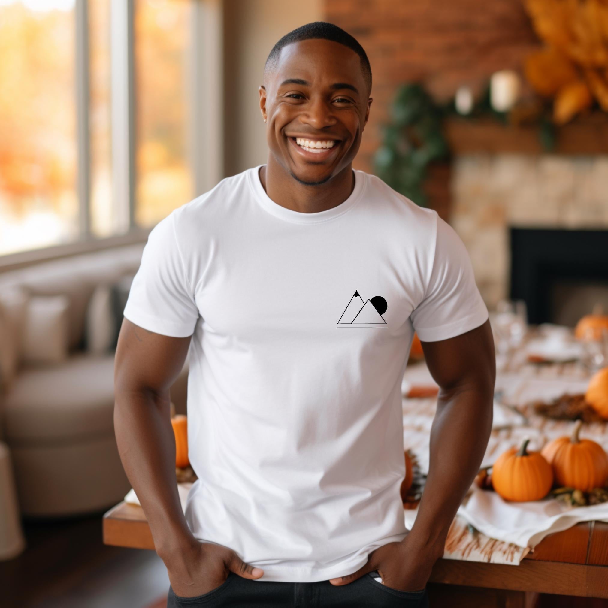 A person wearing a white t-shirt with a simple geometric mountain silhouette on the front, standing in dining room.
