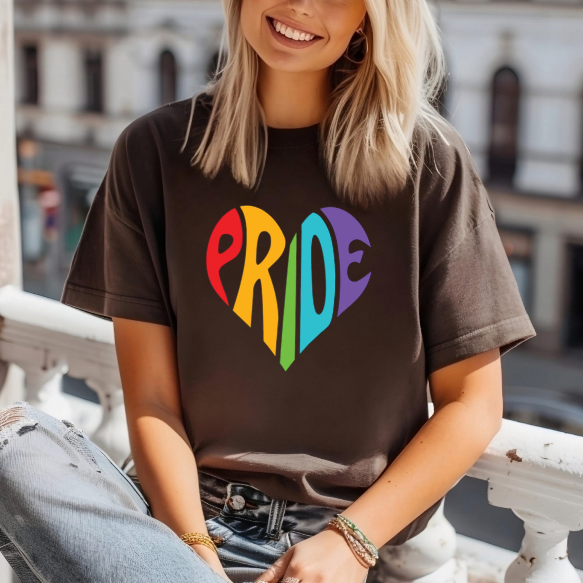 Person wearing a brown t-shirt with 'PRIDE' in colorful letters, sitting on a ledge.