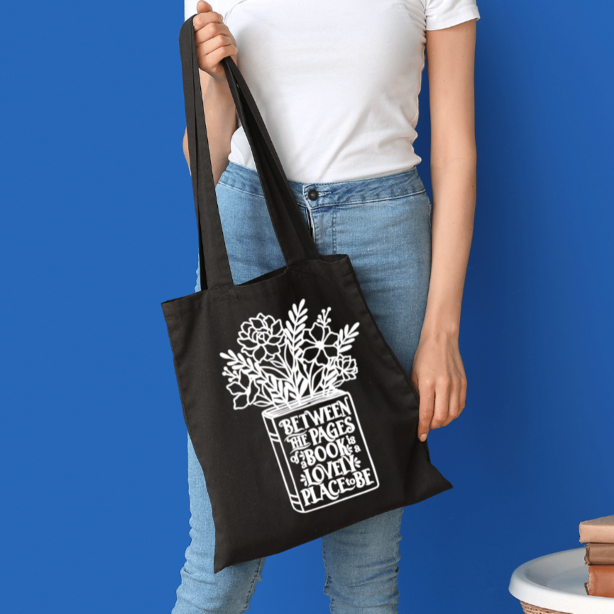 Person holding a black tote bag with a white design against a blue background