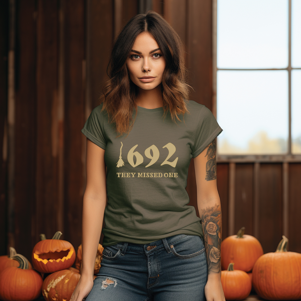 A person standing near pumpkins wearing a green t-shirt with the text '1692 THEY MISSED ONE' on it.