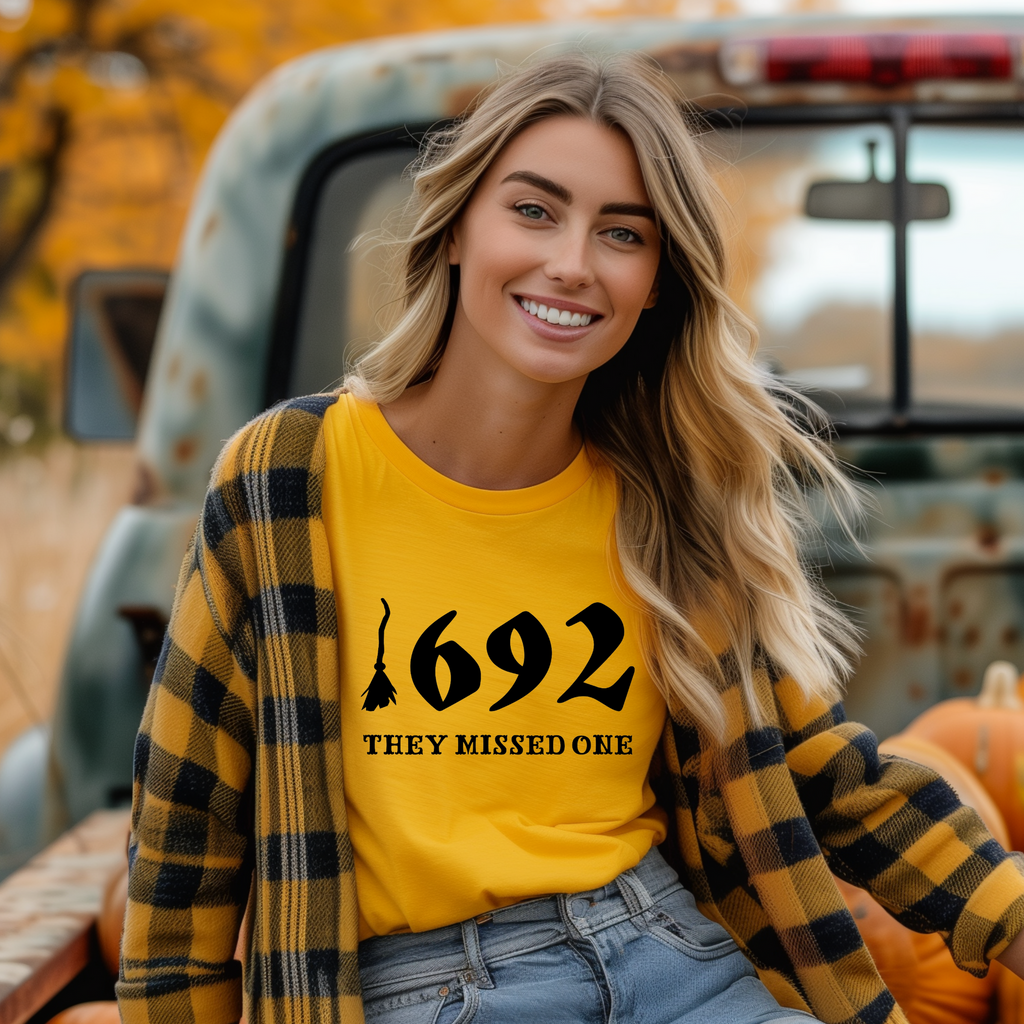 A person sitting in the back of a truck wearing a yellow t-shirt with the text '1692 THEY MISSED ONE' on it.