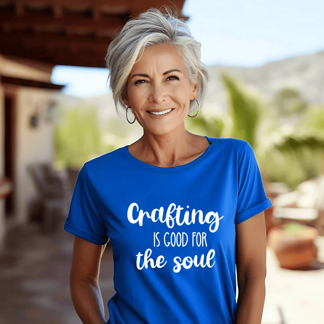Woman wearing a blue t-shirt with 'Crafting is good for the soul' text outdoors.