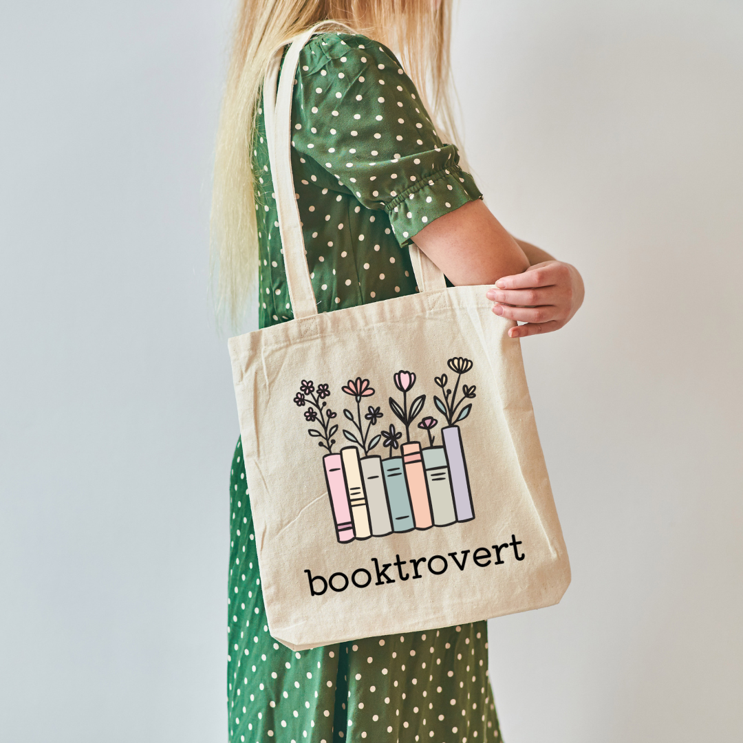 Person holding a tote bag with 'booktrovert' design on a plain background