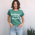 Woman wearing a green t-shirt with 'Crafting is good for the soul' text on a plain background