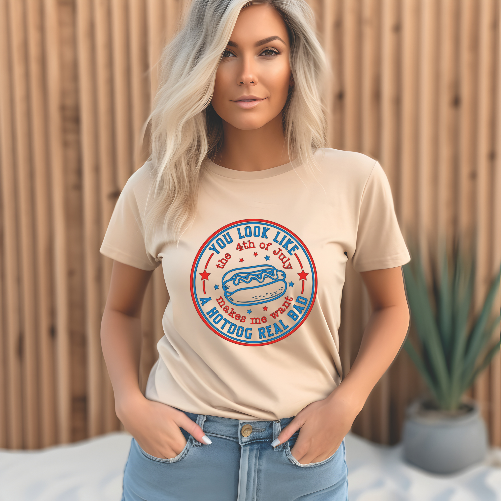 Woman wearing a beige t-shirt with a graphic design in front of a wooden fence.