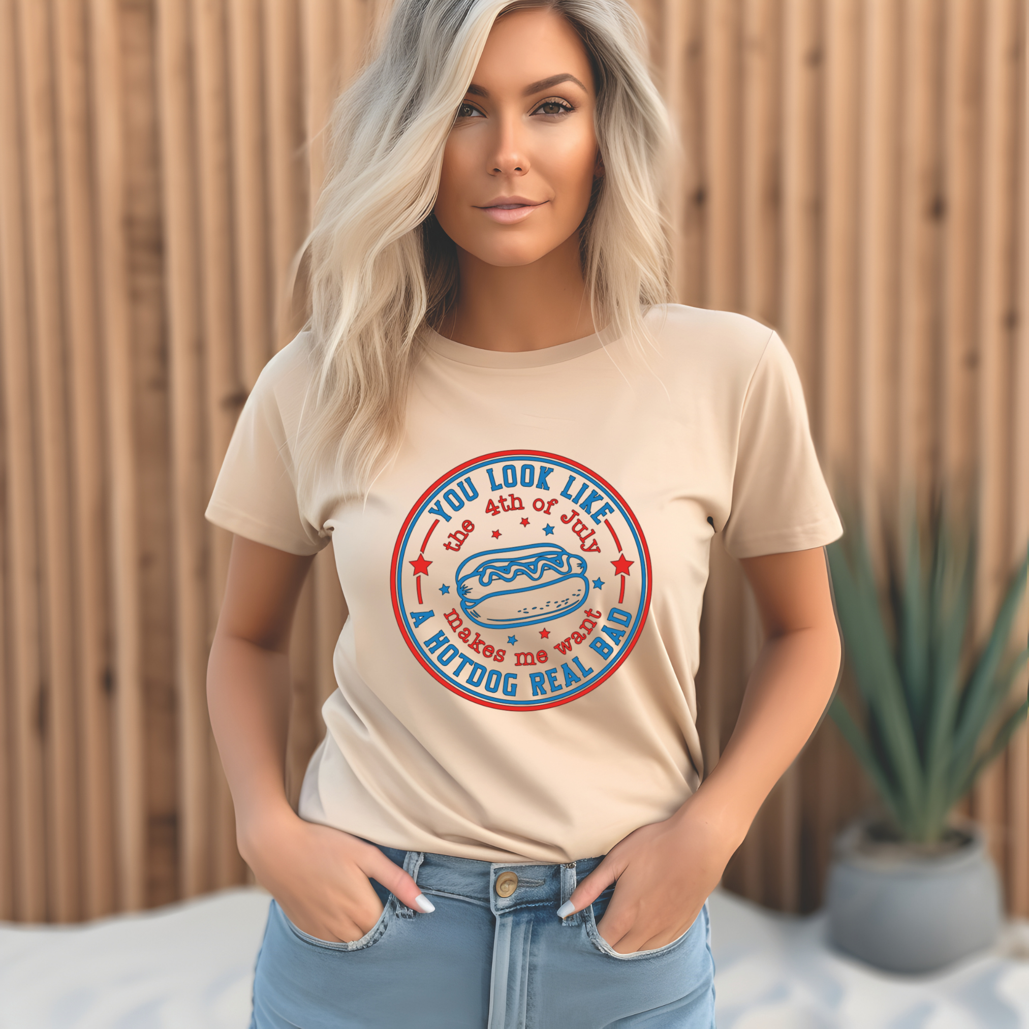 Woman wearing a beige t-shirt with a graphic design in front of a wooden fence.