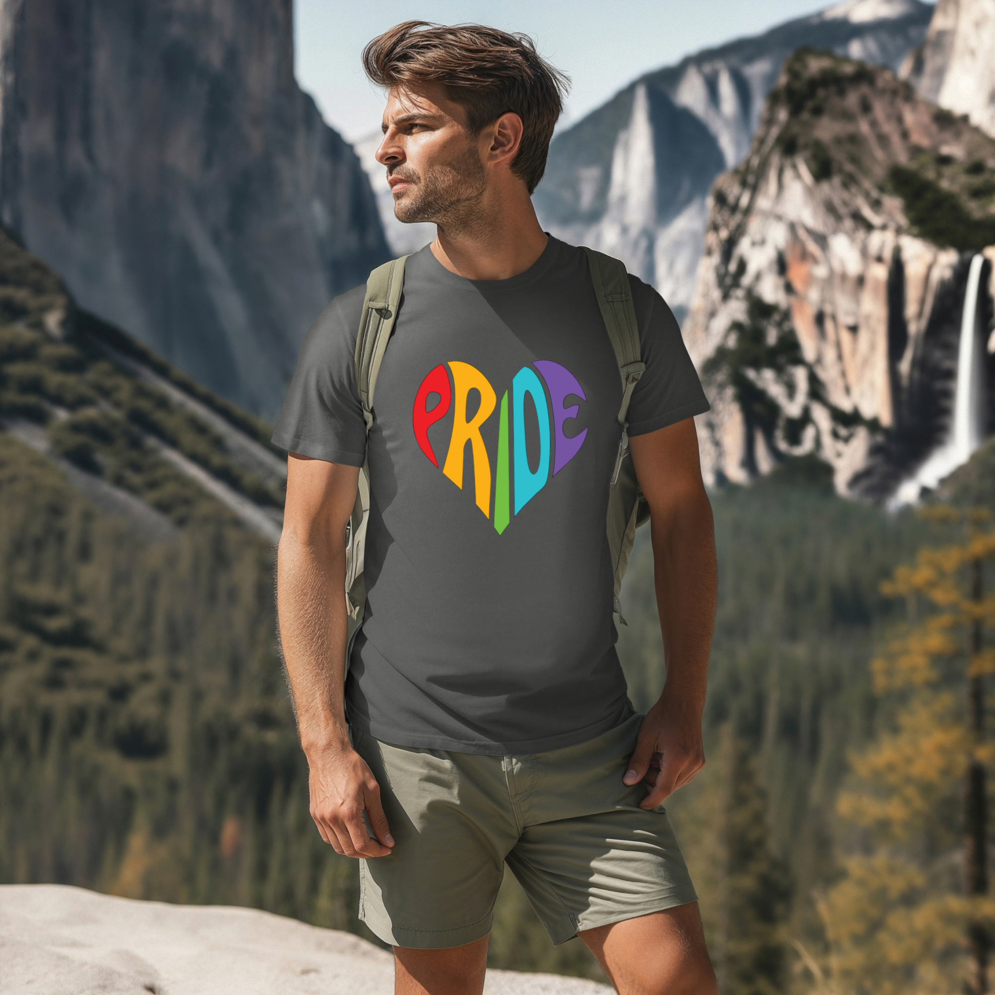 Man wearing a 'PRIDE' t-shirt with colorful letters in a heart shape, standing in a mountainous landscape.