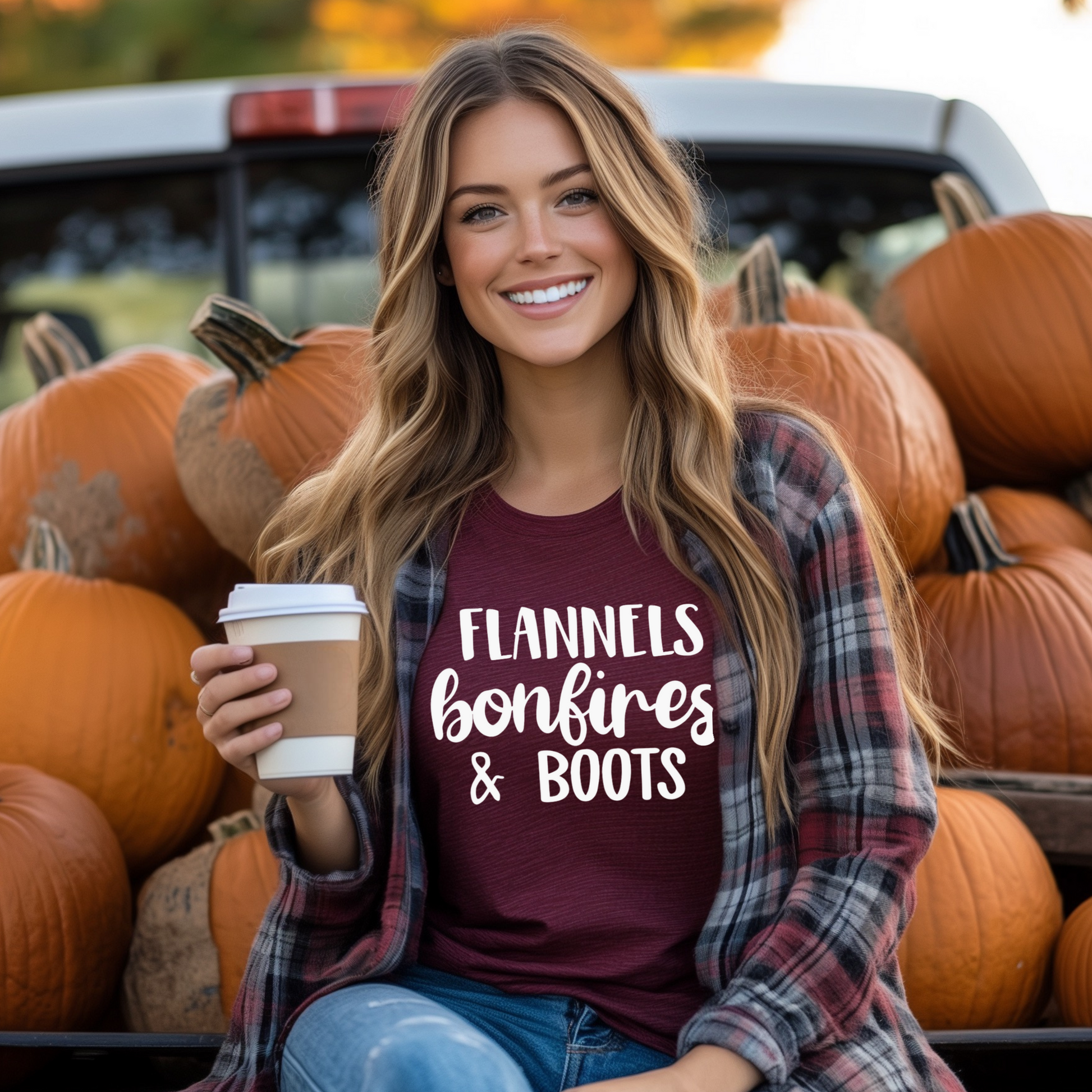 A woman smiling and sitting in a truck, wearing a green t-shirt with the text 'FLANNELS BONFIRES & BOOTS' printed on it, surrounded by pumpkins.