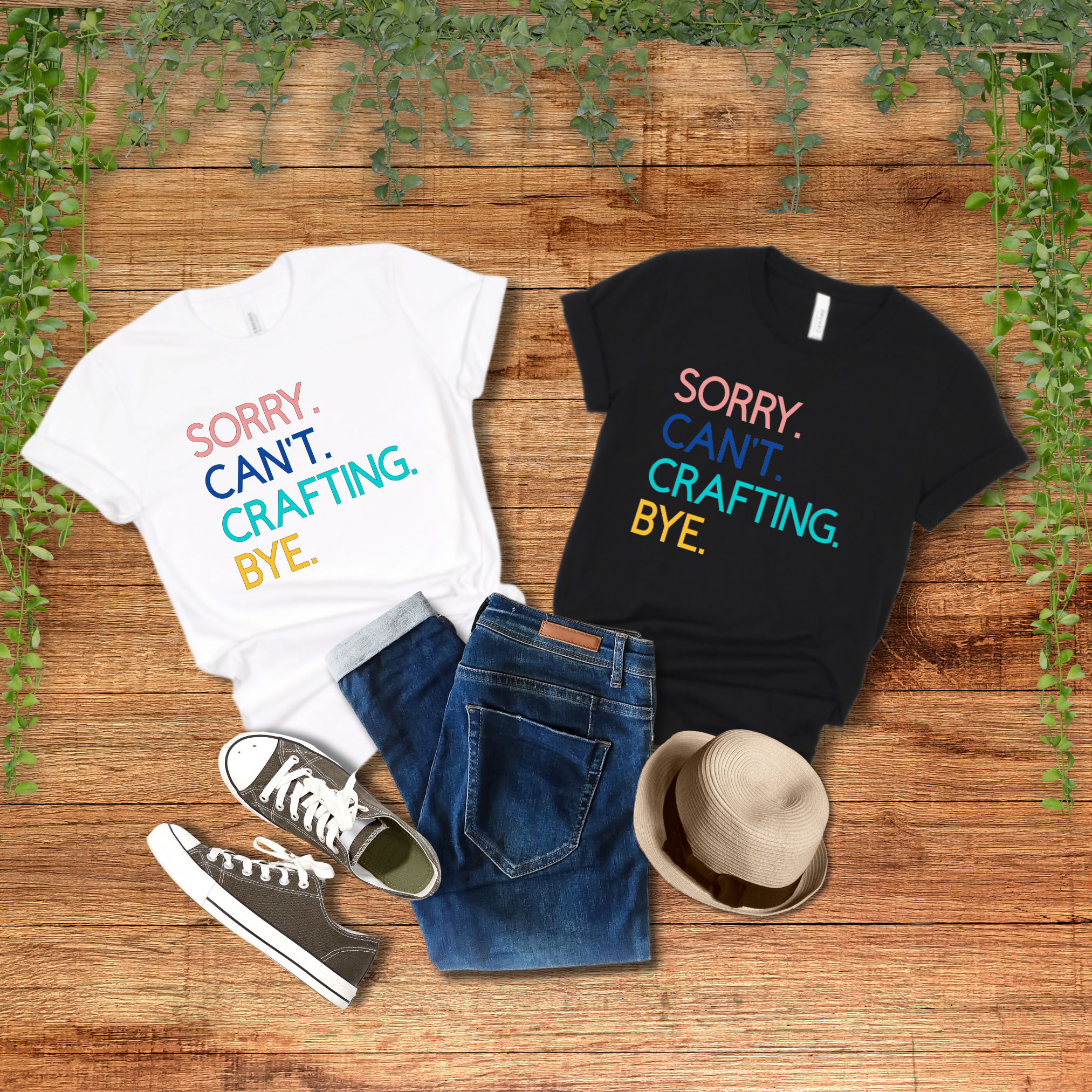 Two shirts laying on a wooden background, one white and one black, both with the text 'Sorry. Can't. Crafting. Bye.', each line with a different color text. Shoes, denim pants, and a hat displayed alongside. 