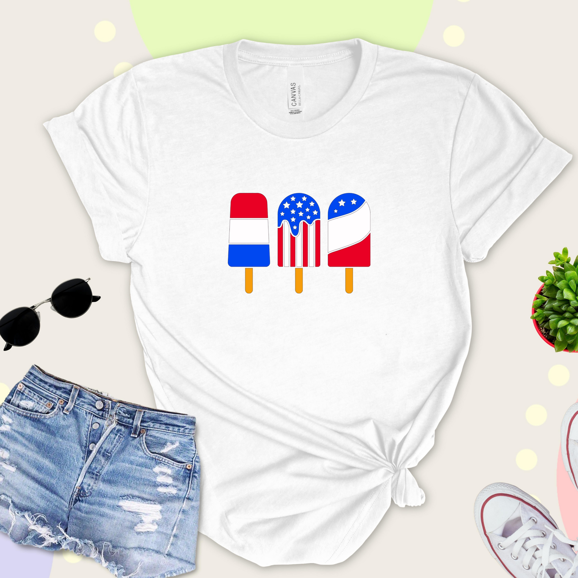 White t-shirt with colorful popsicle design, paired with denim shorts on a light background.