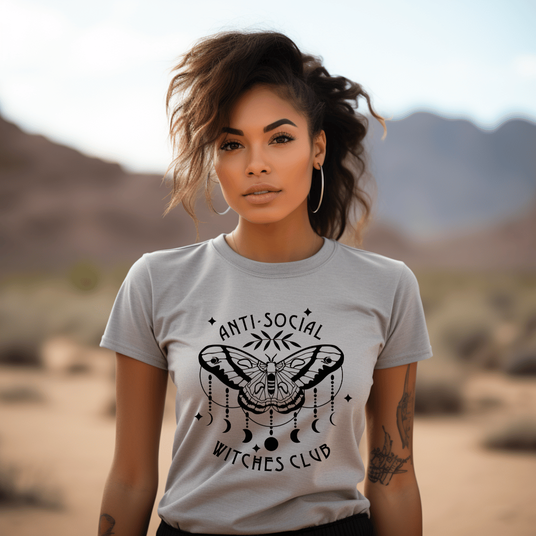 Woman wearing a light grey t-shirt with 'Anti-Social Witches Club' design in a desert setting