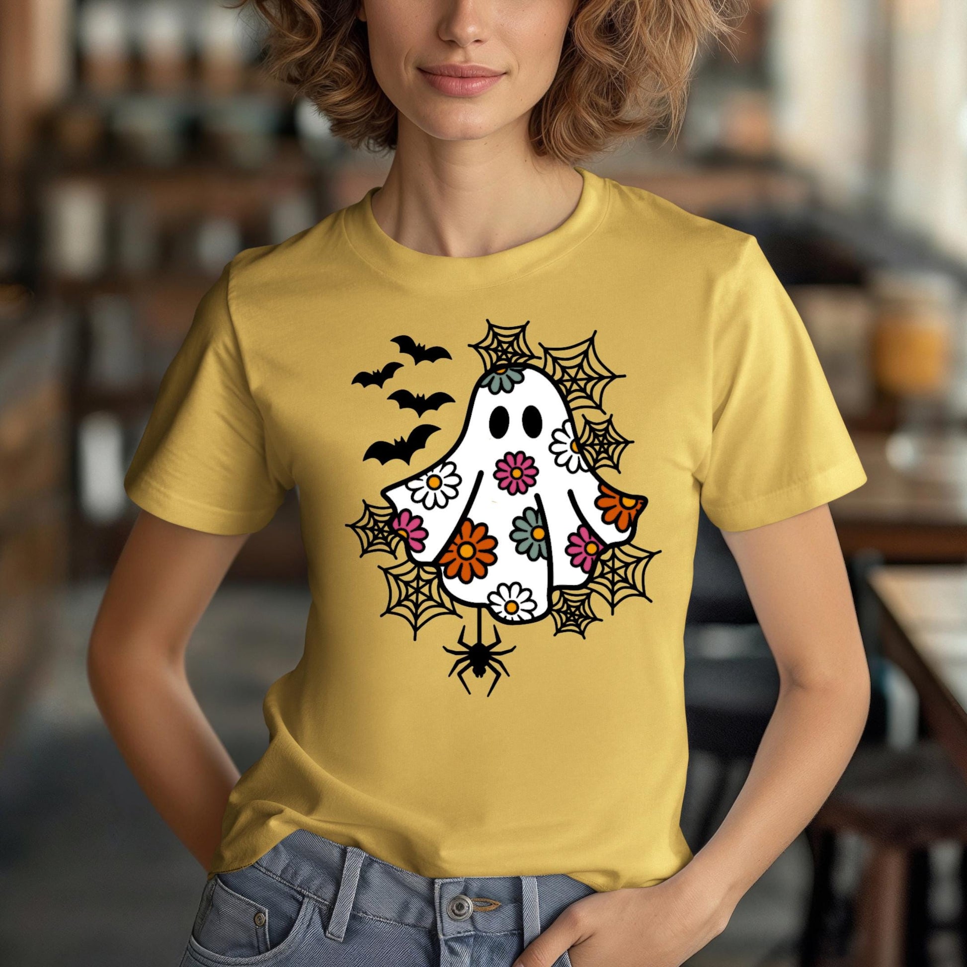 A woman wearing a yellow t-shirt with a whimsical design featuring a ghost, bats, and spiders on it.
