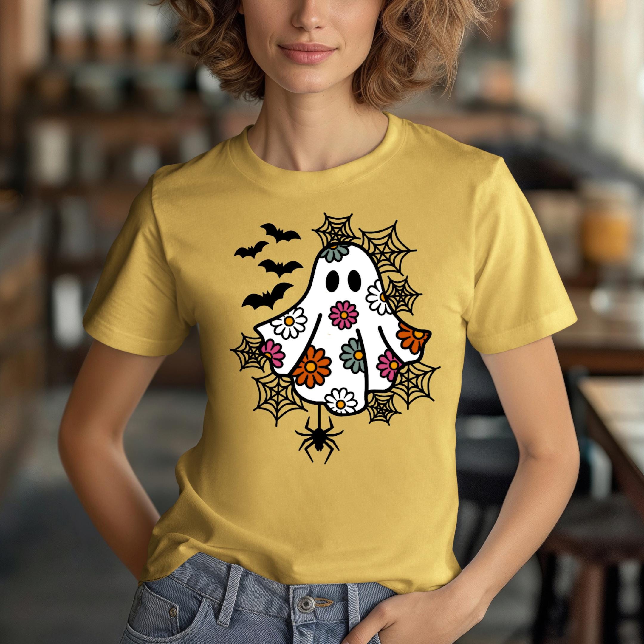 A woman wearing a yellow t-shirt with a whimsical design featuring a ghost, bats, and spiders on it.