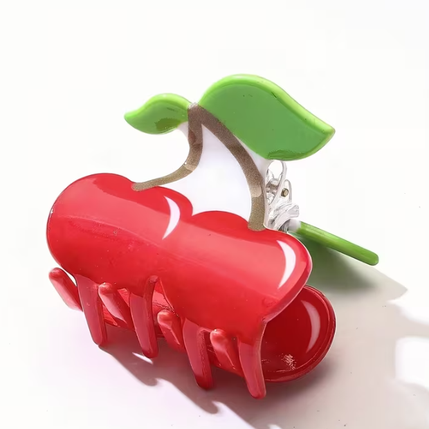 Red hair clip shaped like a cherry with a green leaf on a white background