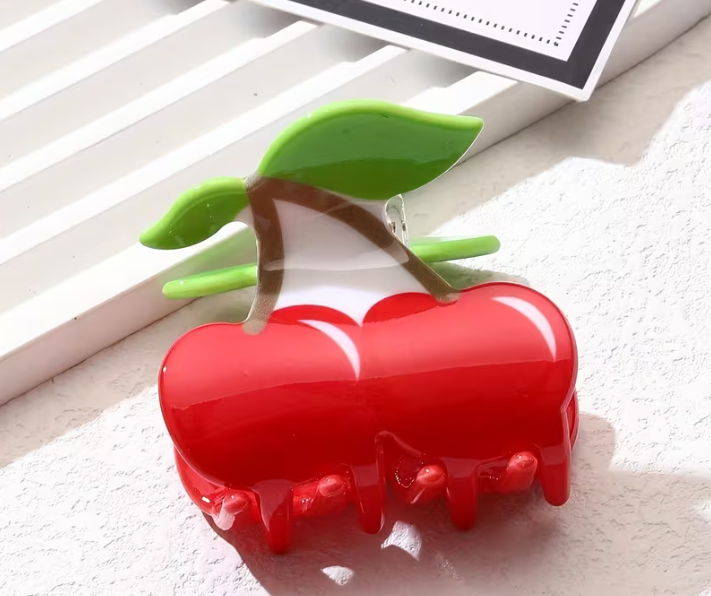 Red hair clip shaped like a cherry on a white background