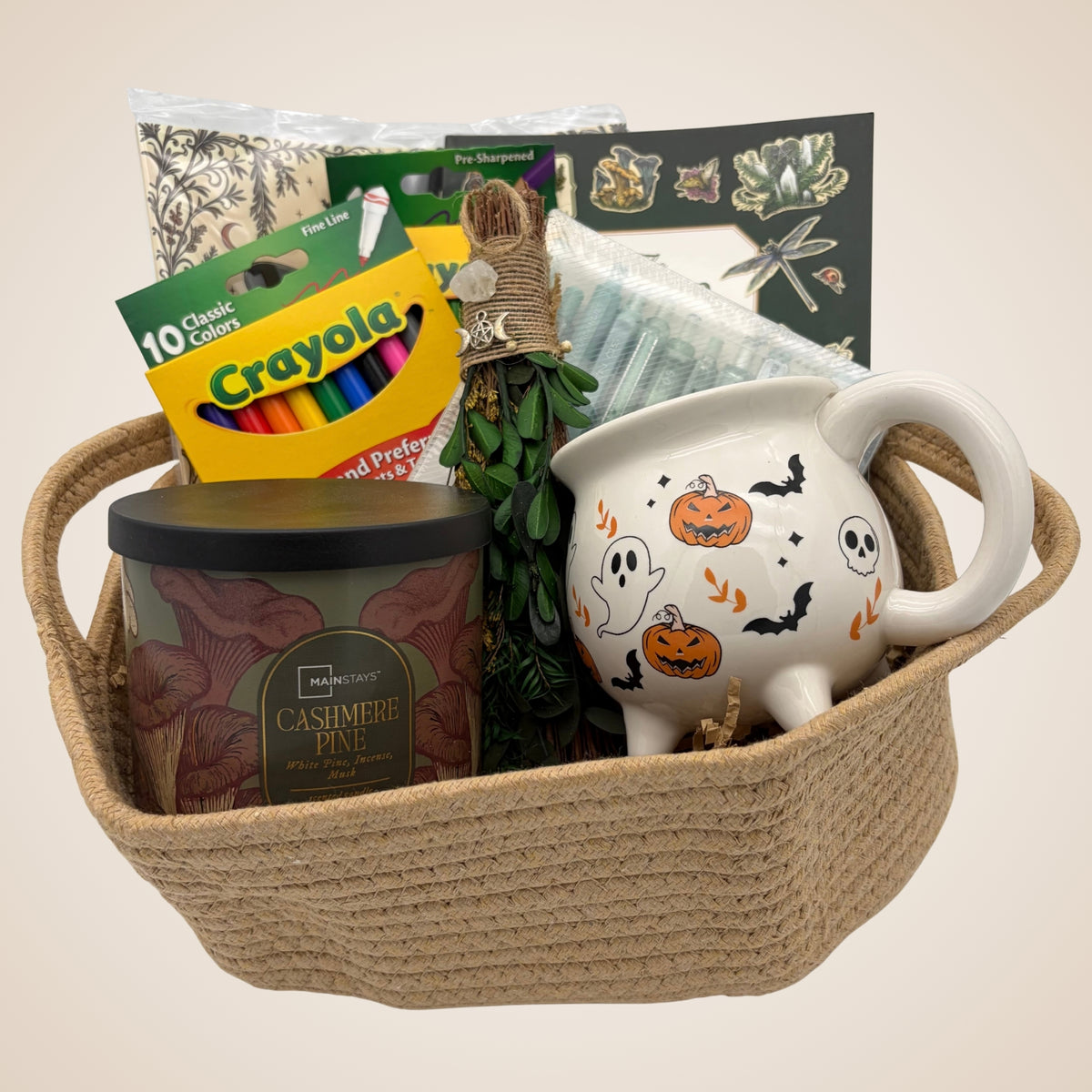 Cottage witch coloring book gift set in a jute rope basket with a cauldron mug, mushroom-print candle, mini broom, and art supplies