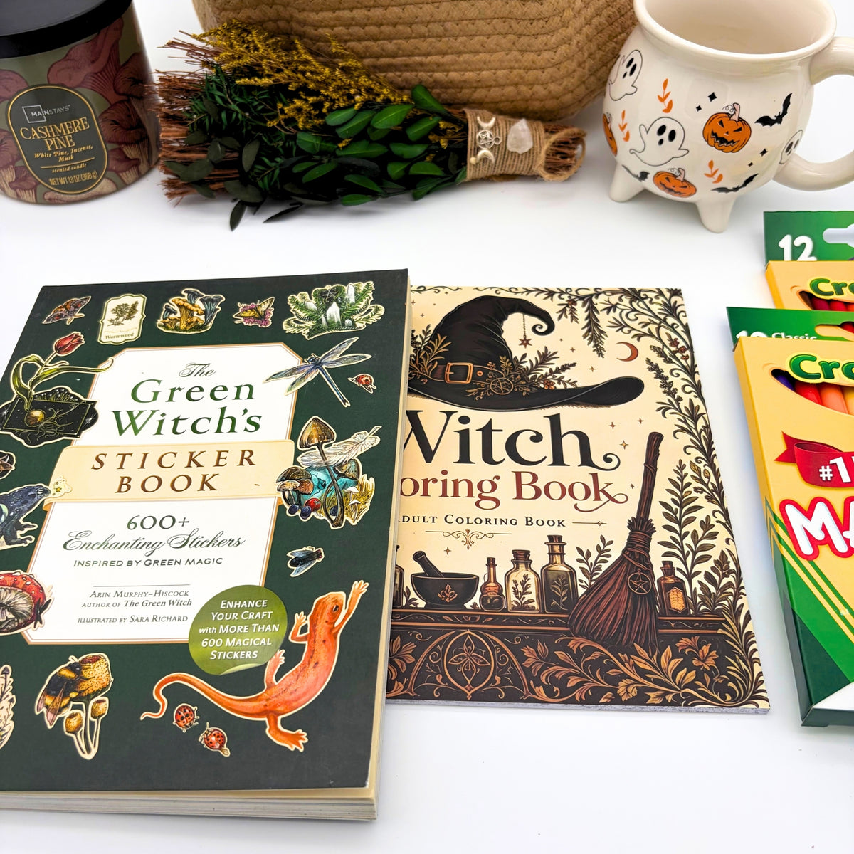 Flat lay of the green witch sticker book, witch coloring book, markers, and colored pencils with the candle, broom, basket, and mug