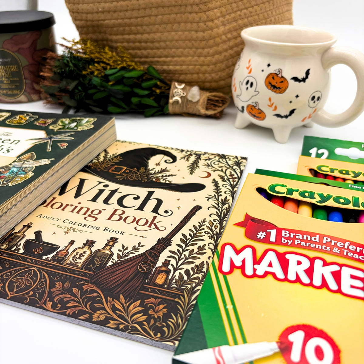 Witch adult coloring book cover with a witch hat, potion bottles, and botanical borders beside the sticker book, markers, and pencils