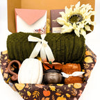 Close view of the olive green cozy fall gift box showing the knit throw blanket, pumpkin mug with gold spoon and crocheted pumpkin coaster
