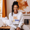 "Fall Vibes" with "Fall" in orange block letters and "Vibes" in navy script above a decorative orange and navy leaf on a white sweatshirt