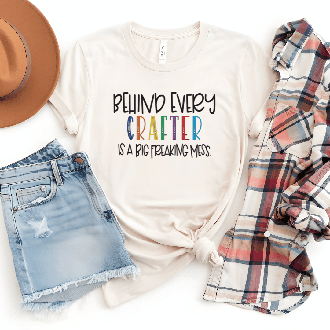 Behind Every Crafter Is A Big Freaking Mess funny t-shirt in a light tan color with rainbow lettering