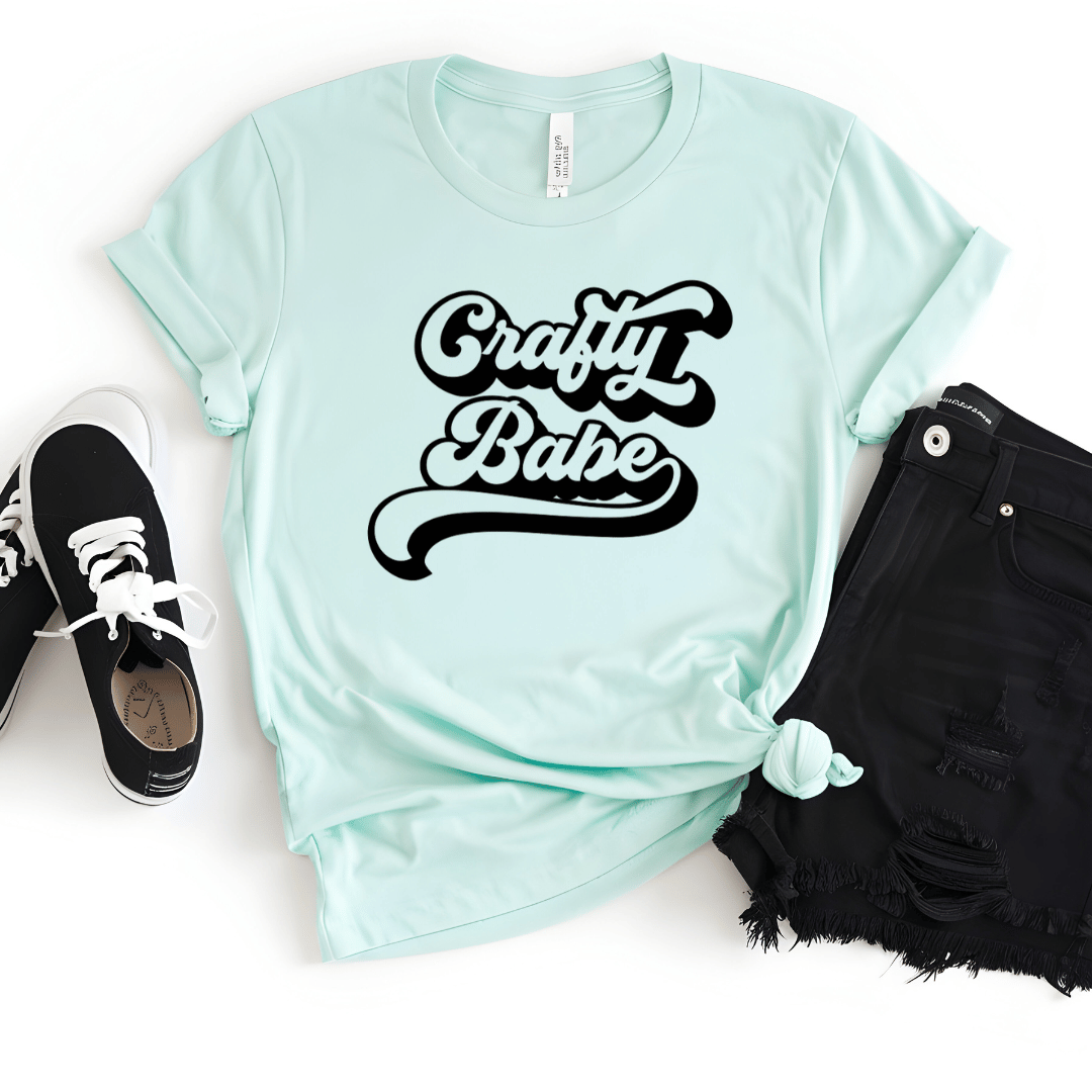 Mint green t-shirt with 'Crafty Babe' text, paired with black shorts and sneakers on a white background