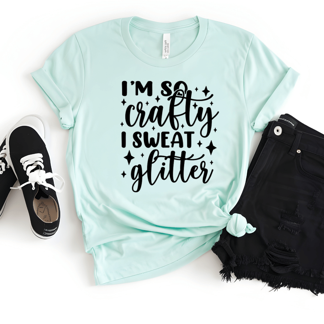 Mint green t-shirt with 'I'm so crafty I sweat glitter' text, paired with black shorts and sneakers on a white background.