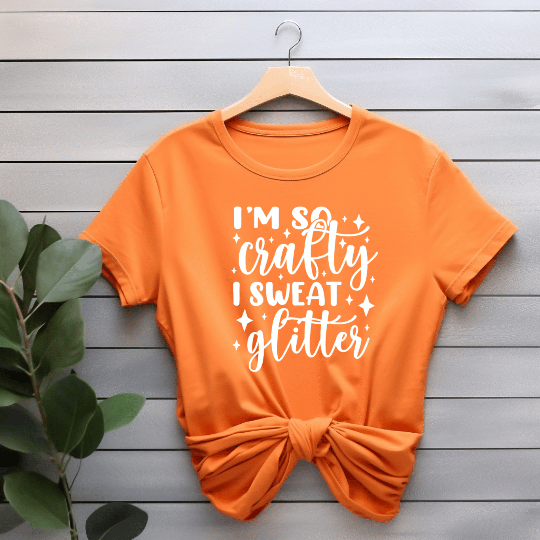 Orange t-shirt with 'I'm so crafty I sweat glitter' text on a wooden background