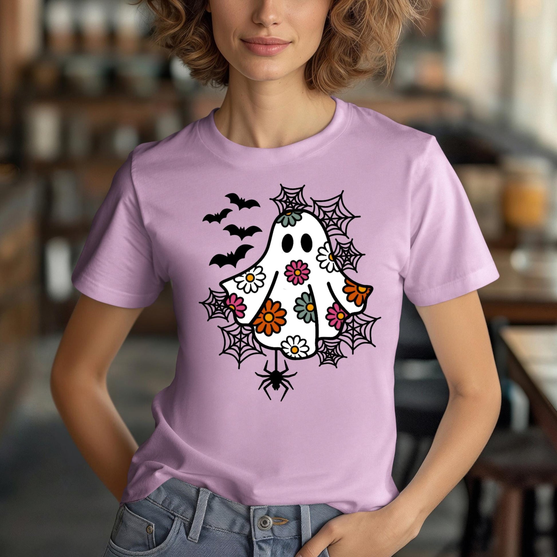 A woman wearing a purple t-shirt with a whimsical design featuring a ghost, bats, and spiders on it.